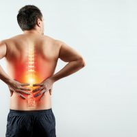 Rear view, the man holds his hands behind his back, pain in the back, pain in the spine, highlighted in red. Light background. The concept of medicine, massage, physiotherapy, health.
